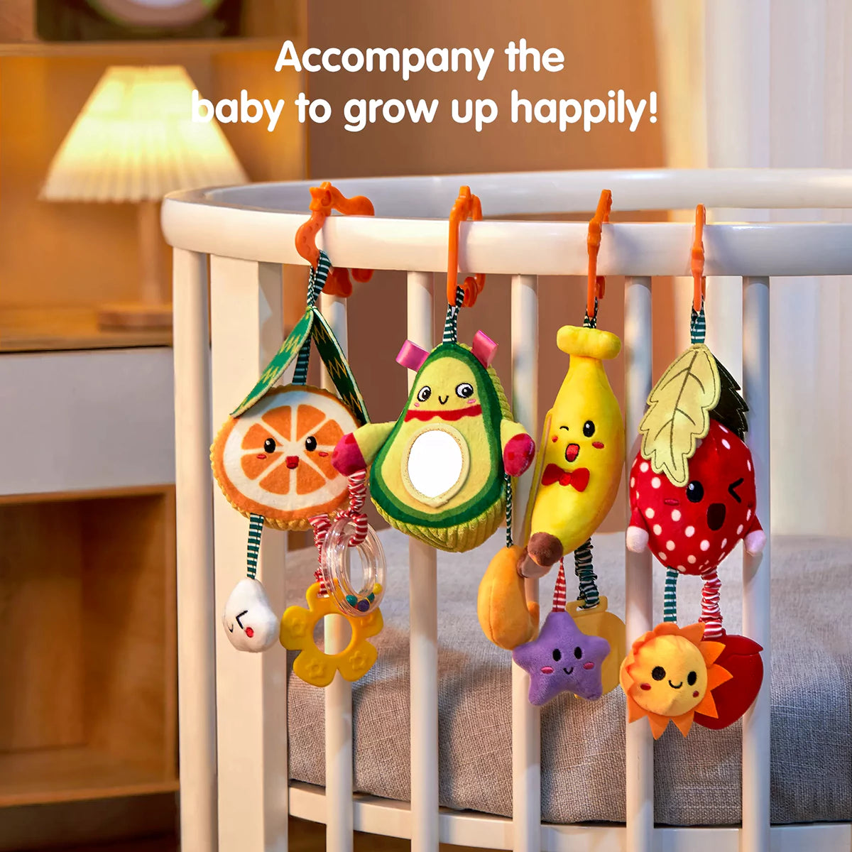 Set of colorful plush fruit-shaped rattle toys (orange, avocado, banana, and strawberry) hanging on a white crib rail. Each toy features cute embroidered faces, mirrors, and dangling accessories, designed to entertain babies while supporting sensory development and happy growth.